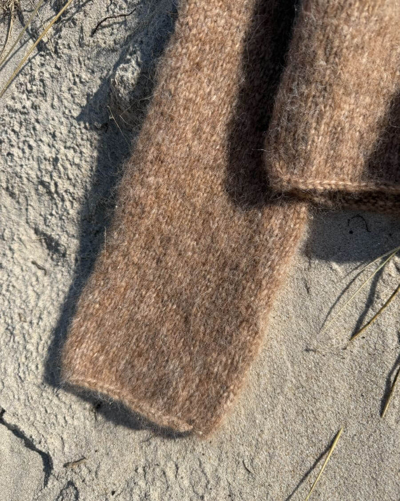 Detaljebillede af ærmet på brun Ivy Sweater liggende i sandet