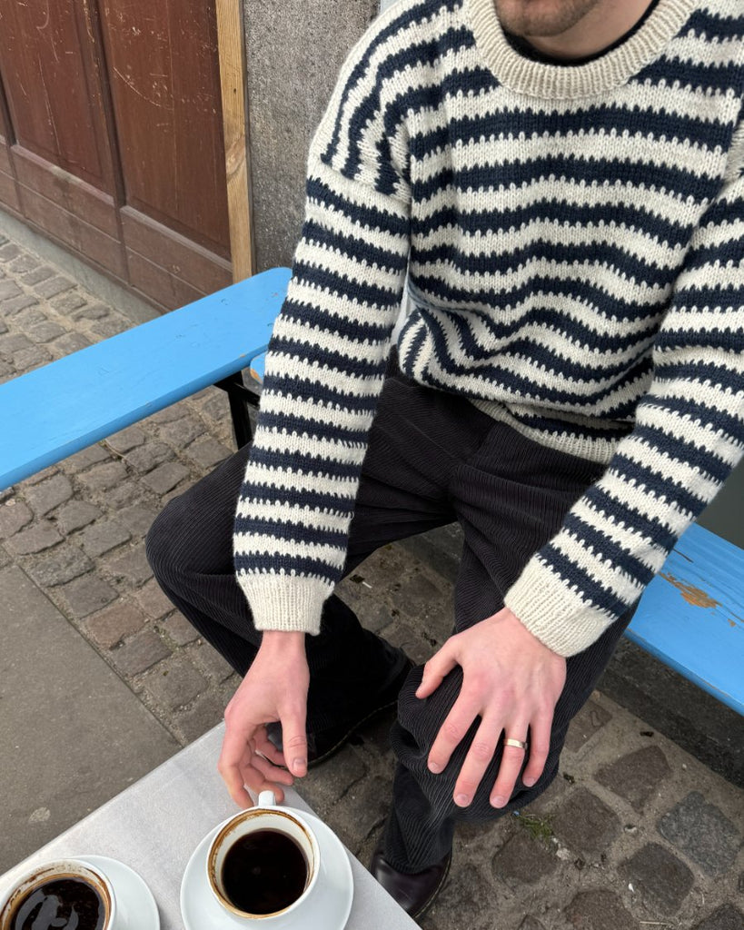 Mand iført hvid og blå Otto Sweater Man rækker ud efter kaffe