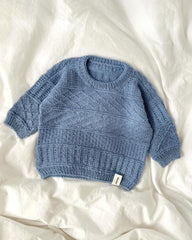 Lyseblå Storm Sweater Baby liggende på sengetøj