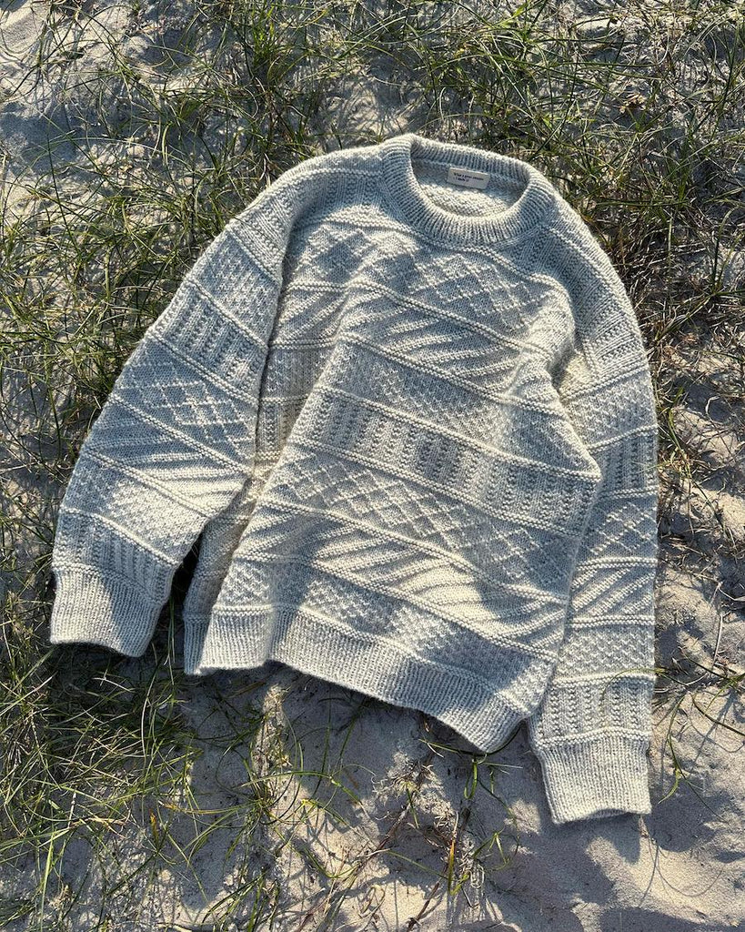 Lysegrå Storm Sweater liggende på sand